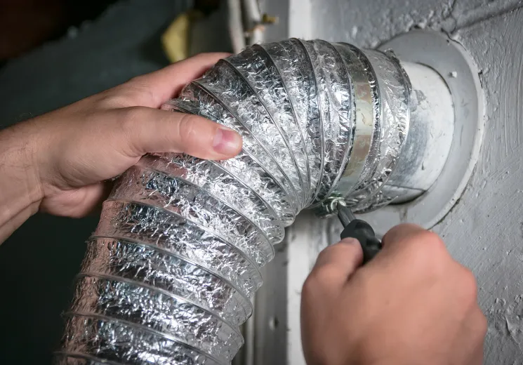 dryer-vent-repair-2 Hands securing a flexible dryer vent hose to a wall duct using a screwdriver.